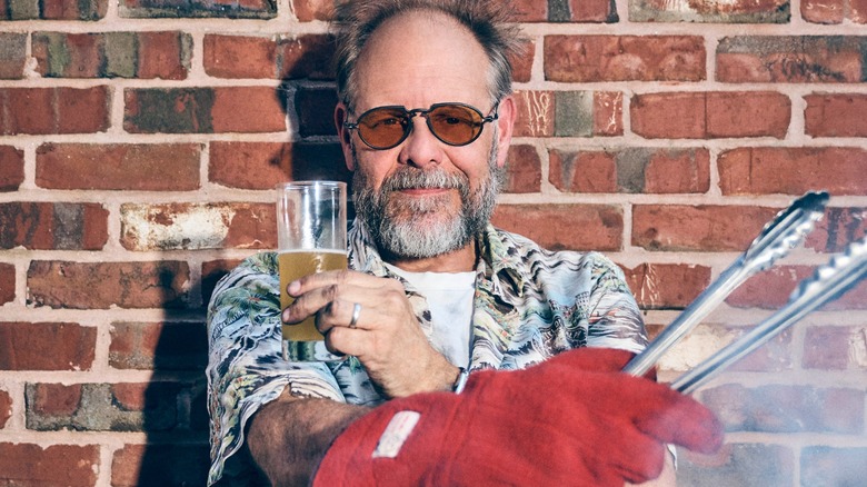 Alton Brown holding tongs and a beer