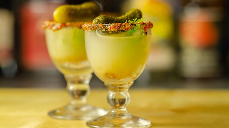 A pickle juice cocktail with a salted and herbed rim, garnished with small, whole pickles.