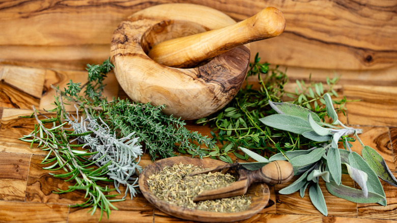 A variety of fresh and dried herbs on a wooden table with a mortar and pestle.