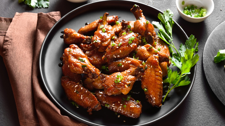 Chinese sticky wings topped with sesame seeds and green onion on a black plate