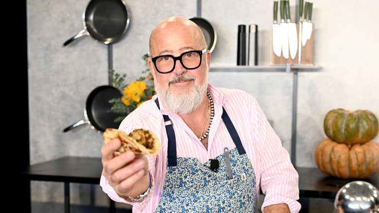 Chef Andrew Zimmern smiling and holding a taco