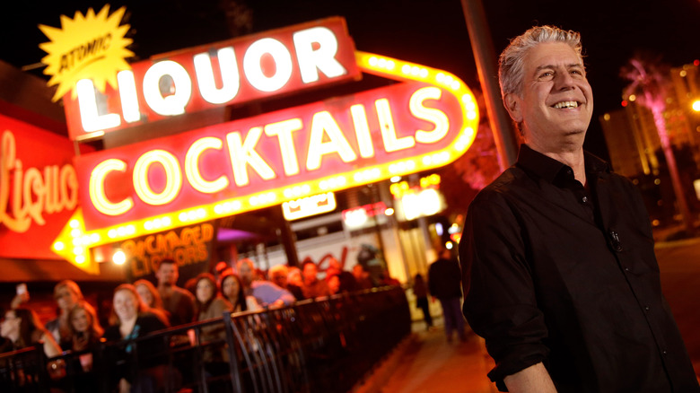 Anthony Bourdain in front of liquor and cocktails sign