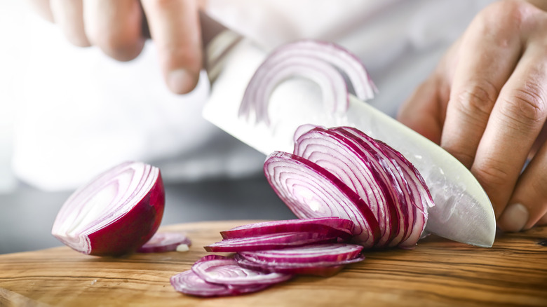 A close-up of hands slicing a red onion with fingers tucked in