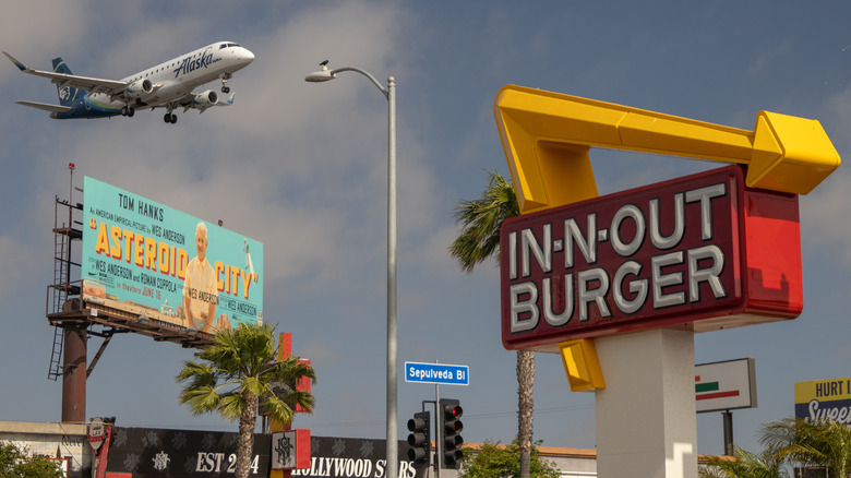 In-N-Out burger sign with a plane flying overhead.