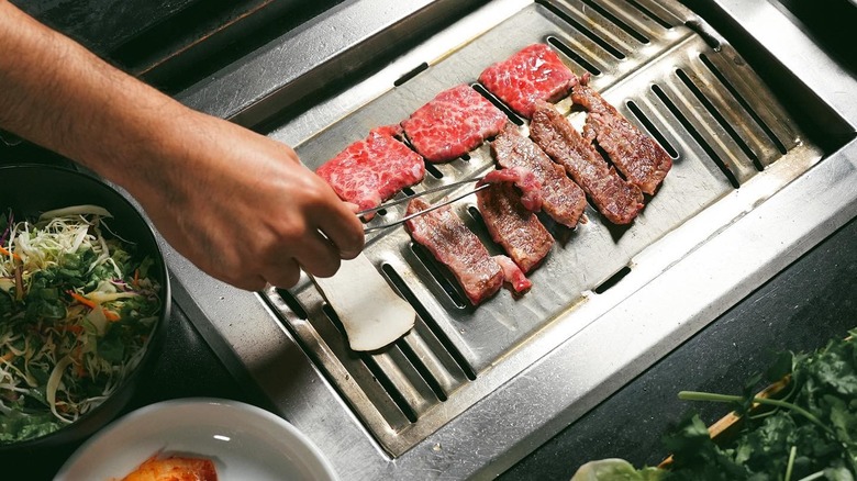 A person putting beef on a grill at Park's BBQ in Los Angeles