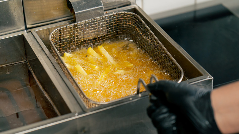 dipping basket of fries into frying oil