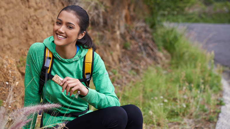 A hiker sits and enjoys a protein bar snack