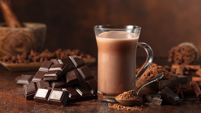 A glass mug of hot chocolate next to bars of chocolate