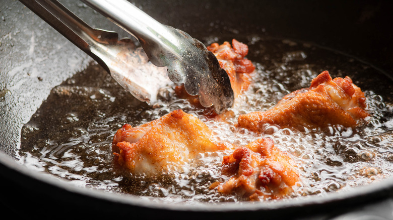 Frying chicken with tongs