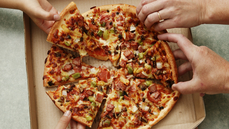 Four hands pulling slices from a pizza in a box