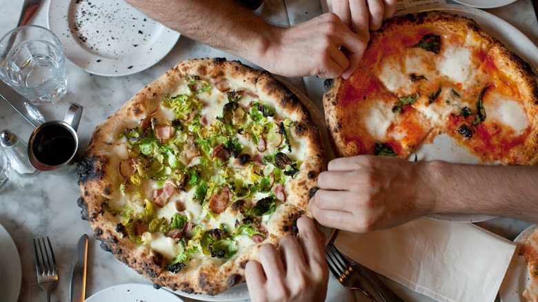 several hands reach in to pull apart gourmet pizza
