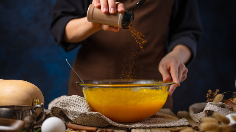 Person seasoning pumpkin pie filling in kitchen