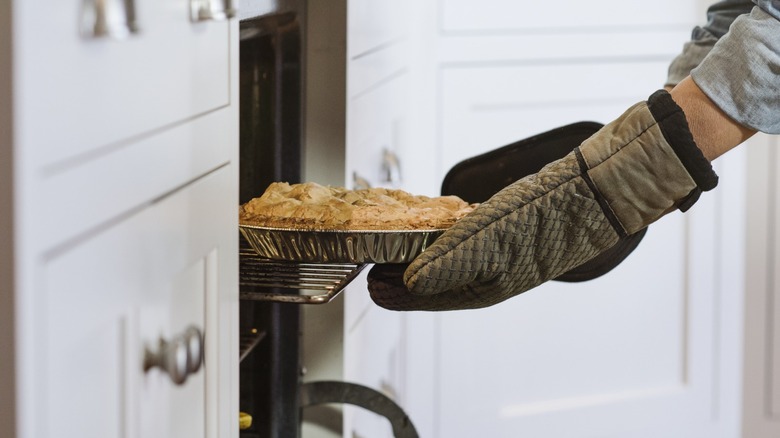 Oven-mitted hands pulling a pie out of the oven