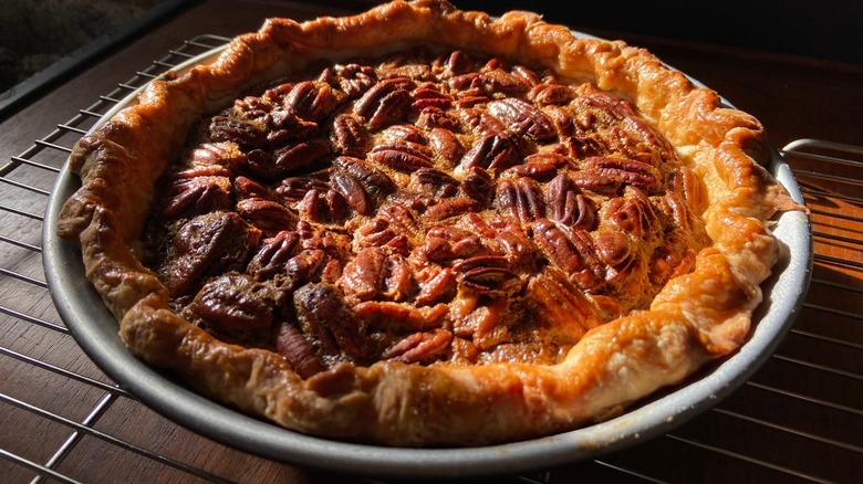 Pecan pie in a metal pie pan on a cooling rack