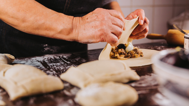 Hands making empanadas on a kitchen surface