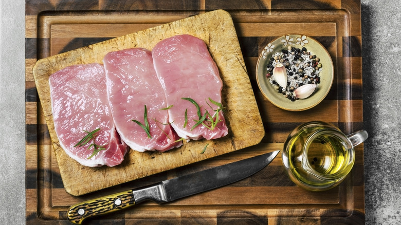 Uncooked pork chops alongside seasoning