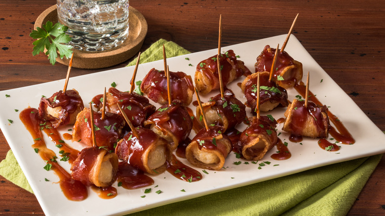 White plate of saucy bacon-wrapped water chestnuts with toothpicks in them