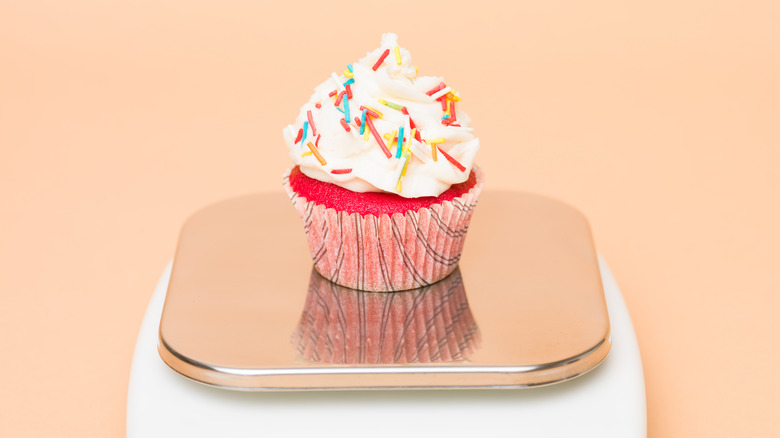 Pink cupcake with sprinkles and white frosting on a kitchen scale