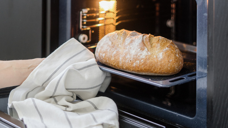 person removing crusty loaf from oven