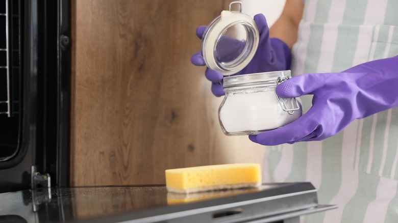 Woman with baking soda and sponge preparing to clean oven