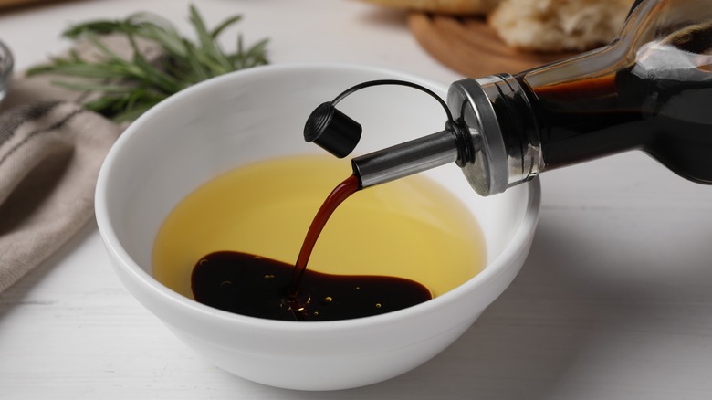 Balsamic vinegar is poured into a small white bowl of olive oil.