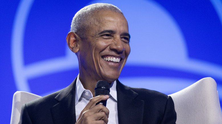 Barck Obama smiling and holding a microphone