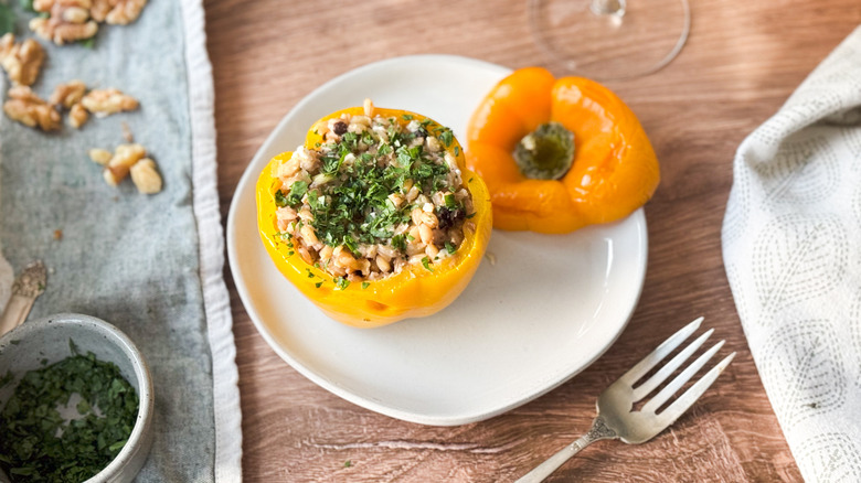 Barley and walnut-stuffed bell pepper on plate with fork and napkin and chopped parsley