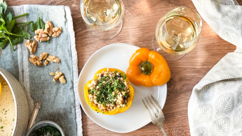 Barley and walnut-stuffed bell pepper on plate with wine glasses, walnuts and parsley