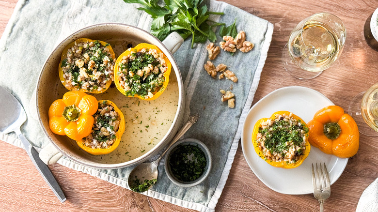 Barley and walnut-stuffed bell peppers in serving dish with garnishes and wine glass