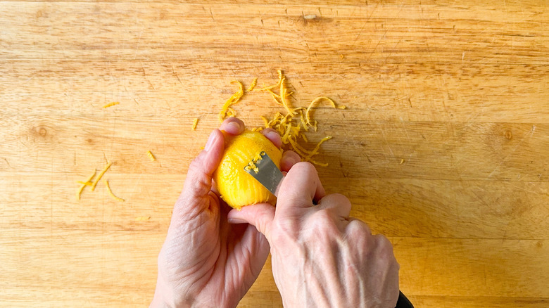 Zesting a lemon with a zesting tool on a cutting board