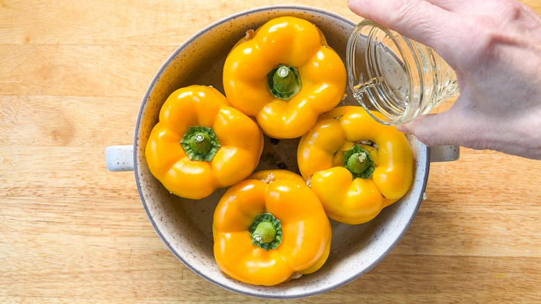 Pouring wine around barley and walnut-stuffed peppers in baking dish