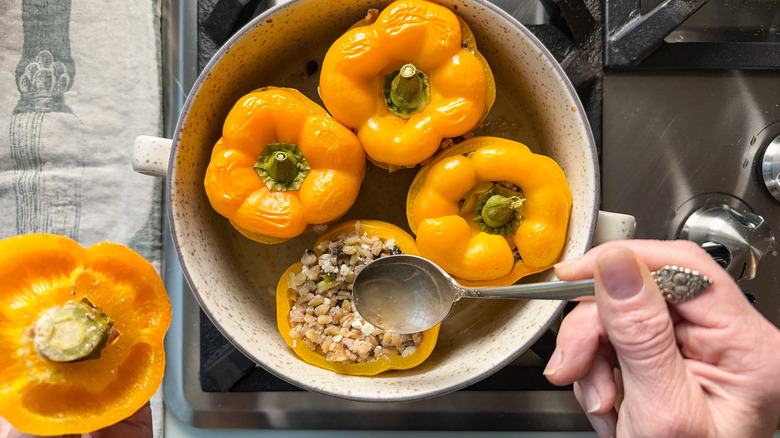 Spooning pan juices over barley and walnut-stuffed bell peppers in baking dish