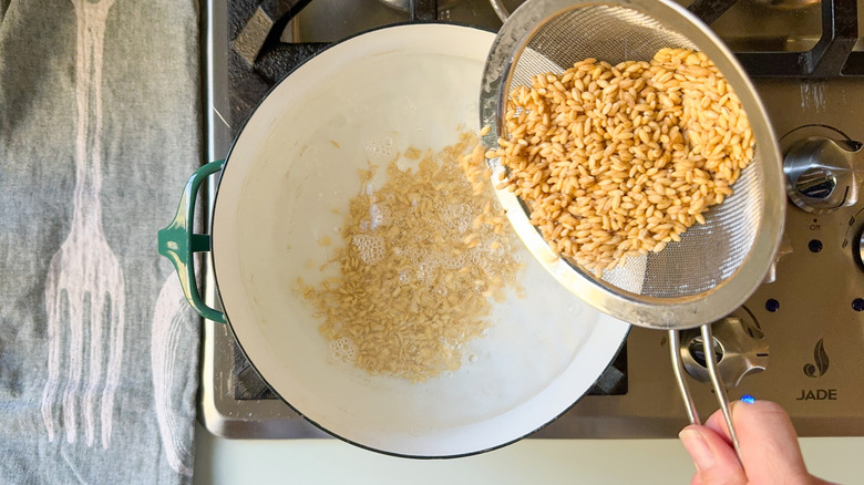 Adding rinsed pearl barley to a pot of water on stovetop