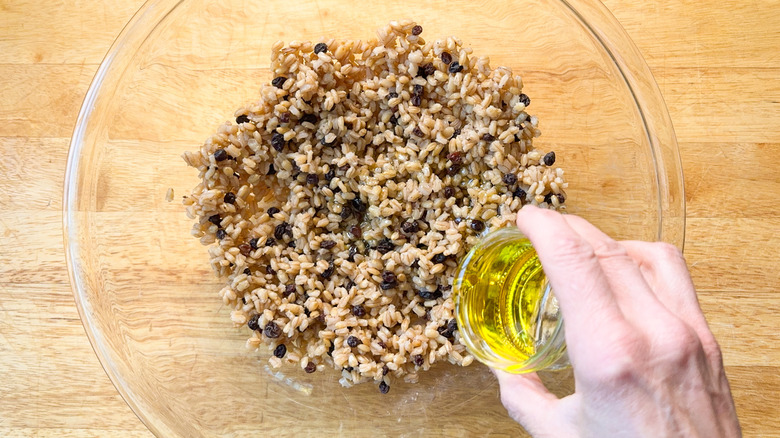 Adding olive oil to cooked pearl barley and currants in large glass bowl