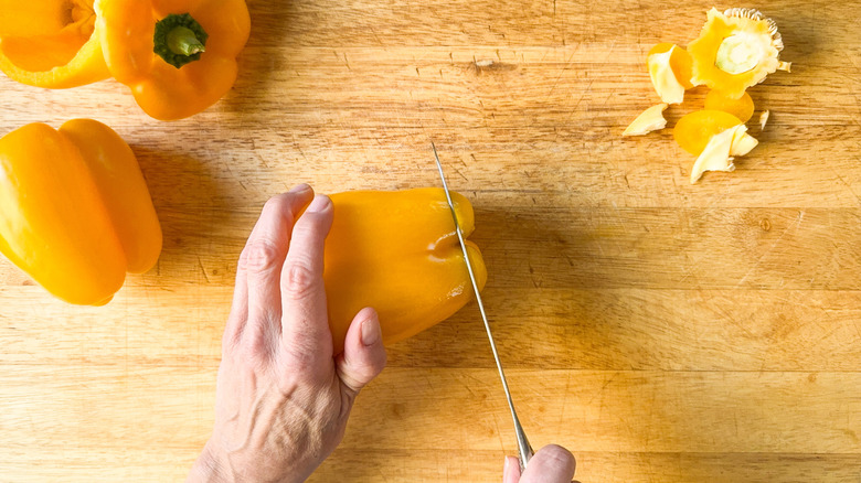 Trimming the bottoms of yellow bell peppers with knife on cutting board