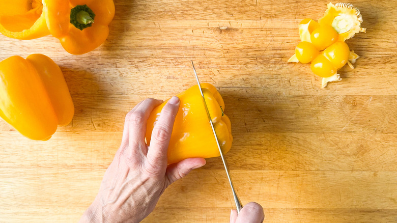 Slicing the top off a yellow bell pepper on a cutting board