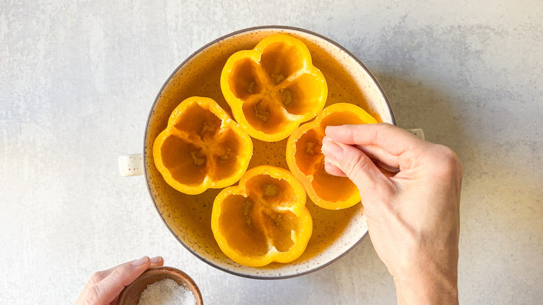 Sprinkling salt inside yellow bell pepper shells in baking dish