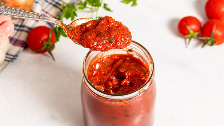 Spoon with tomato sauce over a jar with more tomato sauce