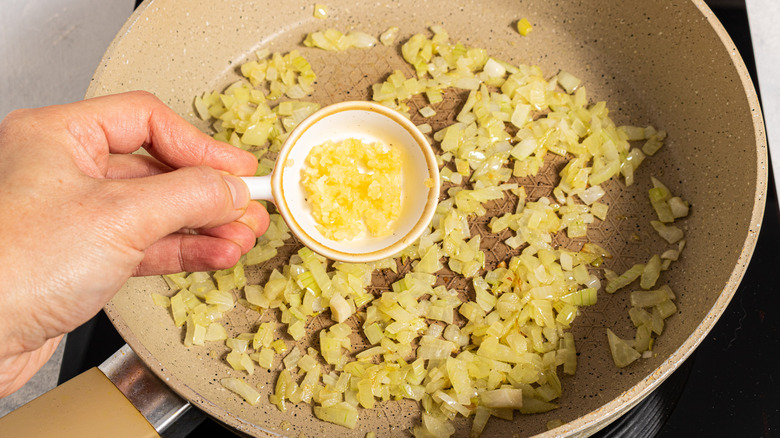 Adding garlic to a skillet with cooked chopped onion