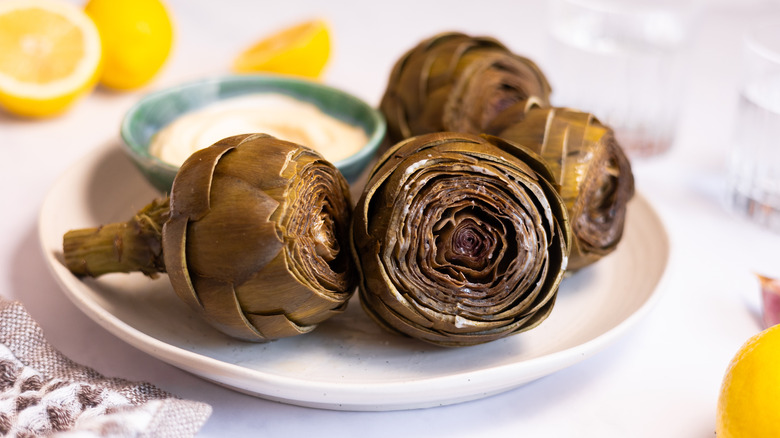 steamed artichokes on plate with bowl of ailoi
