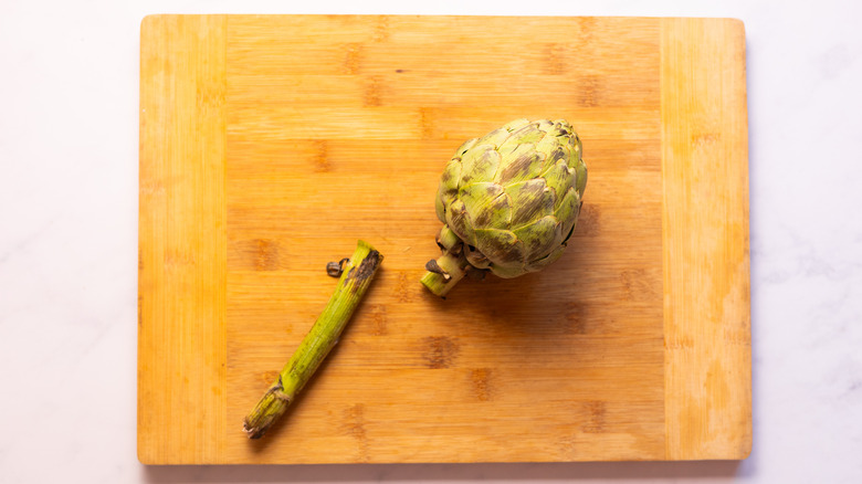 artichoke with stem cut off on wooden board