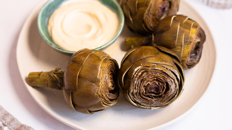 steamed artichokes on plate with bowl of aioli