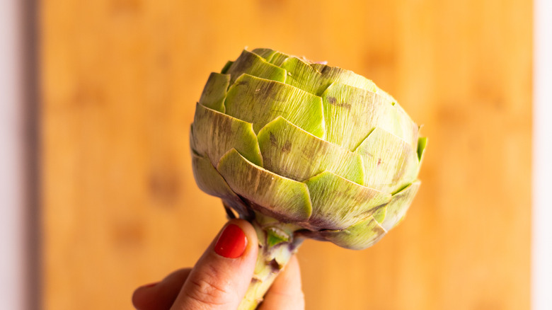 hand holding trimmed artichoke over cutting board