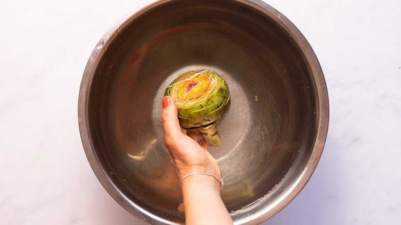 Hand dipping artichoke in bowl of water