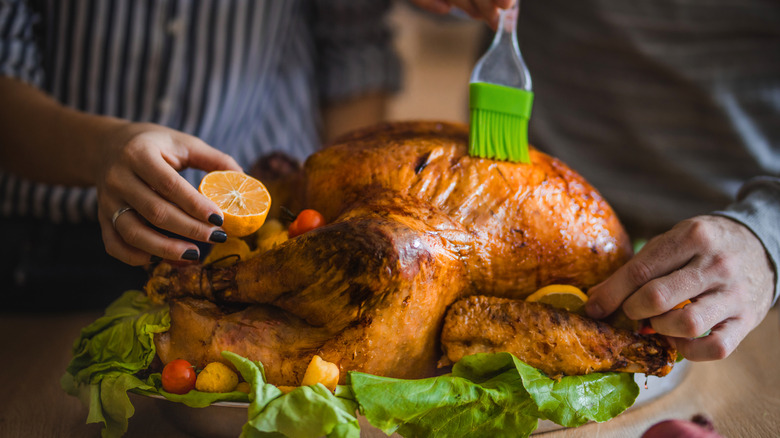 A roasted turkey is getting a brushing of flavor before serving.