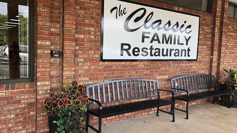 Exterior sign for the CLassic Family Restaurant on a brick wall with black benches below
