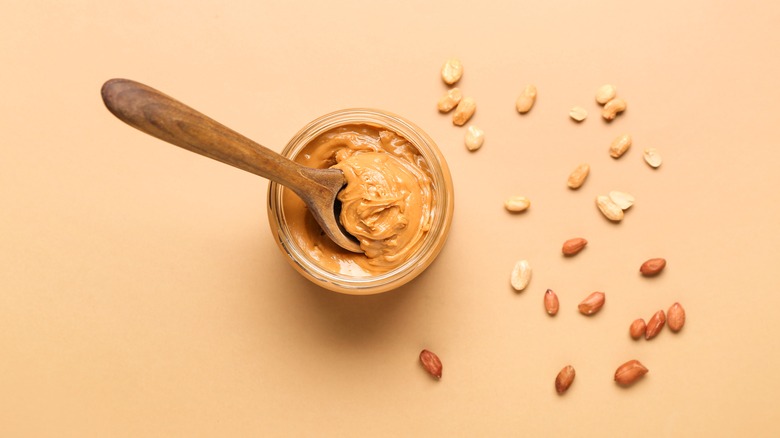 Wooden spoon in jar of peanut butter next to peanuts.