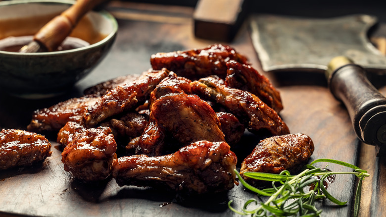 Chicken wings arranged on a cutting board with a bowl of basting sauce in the background
