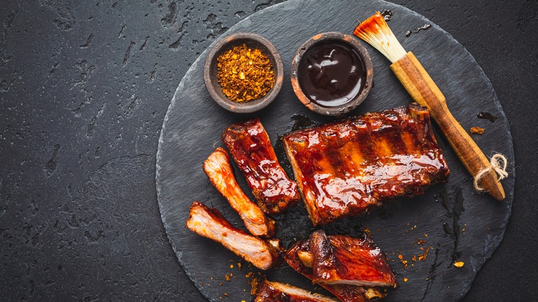 ribs with black sauce glaze alongside two bowls and a brush