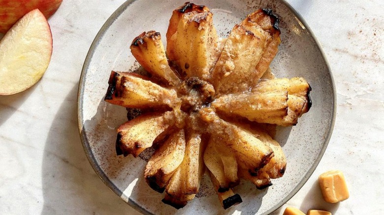 Baked bloomin' apple on a plate next to apple slices and caramels